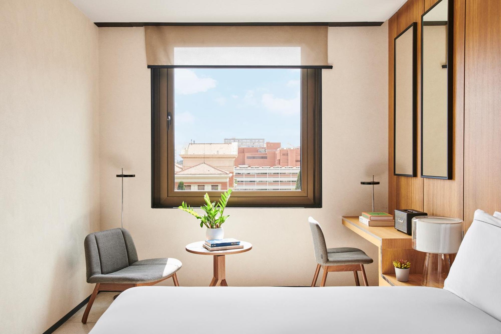 호텔 소피아 바르셀로나 - 인 더 언바운드 컬렉션 바이 하얏트 외부 사진 The photo depicts a modern hotel room with a cozy and minimalist design. There's a large window allowing natural light to enter, showcasing a view of the outside cityscape. In the room, two chairs are positioned near a small round table, which has a 