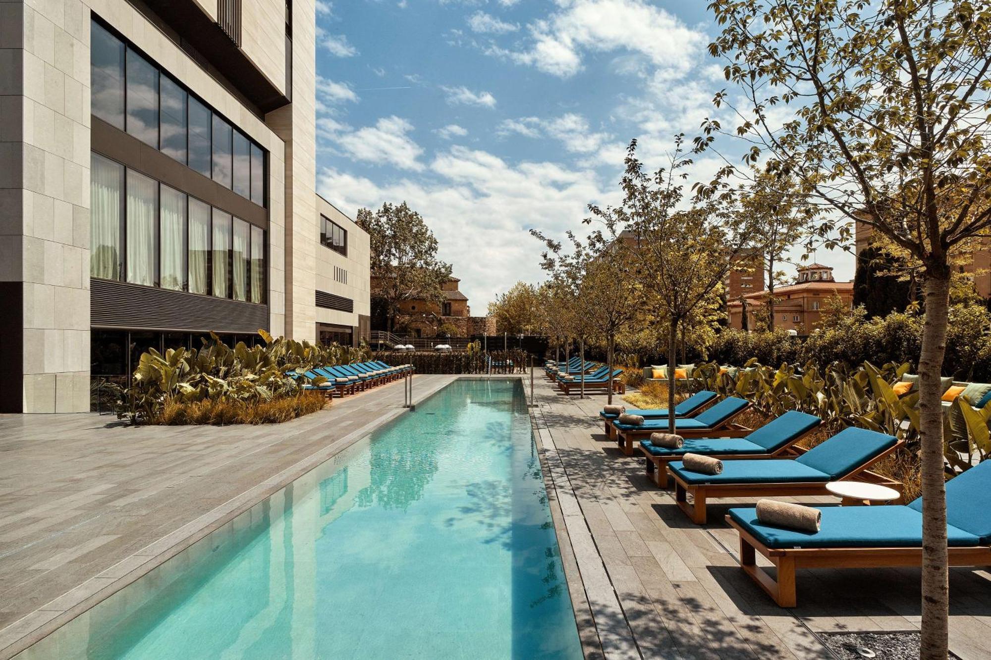 호텔 소피아 바르셀로나 - 인 더 언바운드 컬렉션 바이 하얏트 외부 사진 The photo showcases a modern outdoor pool area. In the foreground, there is a long, rectangular swimming pool with clear blue water. Surrounding the pool are lounge chairs with bright blue cushions, arranged neatly along both sides. The area features